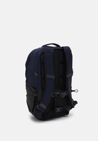 Zaino navy con spallacci imbottiti e base nera. Presenta fibbie regolabili, tessuto testurizzato e una maniglia superiore per un facile trasporto.