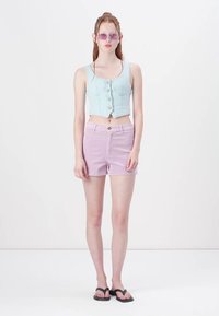 Világoskék farmer crop top gombokkal, amelyet pasztell lila sorttal párosítanak. A modellen áttetsző lila napszemüveg és fekete papucs van.