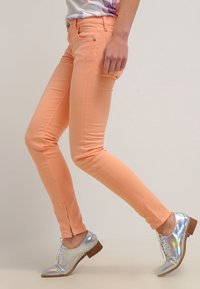 Persikofärgade skinny jeans med dragkedjeanklar och femficksdesign, tillsammans med reflekterande silverfärgade oxfordskor.
