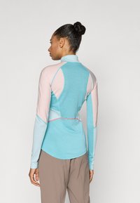 Αθλητική μπλούζα με μακριά μανίκια σε συνδυασμό ανοιχτού μπλε και ροζ, με ψηλό γιακά, raglan μανίκια και ραφές αντίθετου χρώματος. Με λεία υφή.