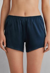 Satinshorts i marinblått med elastisk midja, som har en slät yta och en avslappnad passform, skurna ovanför mitten av låret.