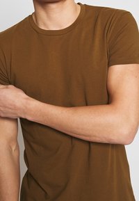 Camiseta de cuello redondo marrón hecha de tela suave, diseño ajustado, mangas cortas y detalles de costura limpios. Textura suave, estilo minimalista.