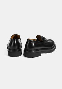 Zwarte leren loafers met een ronde neus, minimale stiksels en een dikke rubberen zool. Het interieur heeft een bruine voering voor contrast.