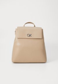 Beige skinnsekk med en strukturert form, forlomma, topphåndtak, sølvlogo og glatt tekstur.
