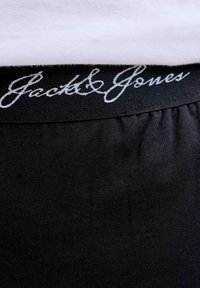 Černé spodní prádlo s texturovaným pasem, na kterém je bílé kurzívou napsané "Jack & Jones", s hladkým povrchem.