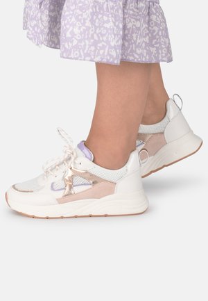 Legs wearing white sneakers with beige and lavender accents paired with a lilac patterned skirt on a plain background.