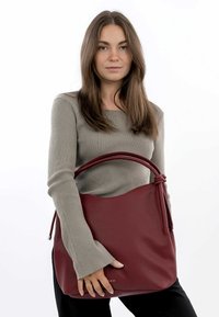 Burgundowa skórzana torba na ramię z teksturowanym wykończeniem, z twisted uchwytem i otwartym projektem, trzymana przez modelkę w swetrze z prążkami.