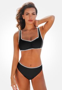 Schwarzes Bikini mit weißem Zickzackbesatz, ausgestattet mit einem quadratischen Ausschnitt und Raffung am Oberteil, ergänzt durch hochgeschnittene Hosen.