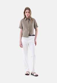 Camicia a maniche corte, verde oliva, con bottoni, realizzata in un tessuto testurizzato, abbinata a pantaloni bianchi a gamba dritta e sandali neri con cinturini bianchi.