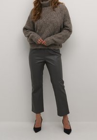 Gruby sweter z golfem w jasnoszarym kolorze, zestawiony z ciemnoszarymi, wysokimi, krótko przyciętymi spodniami z imitacji skóry oraz czarnymi szpilkami w szpic.