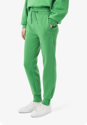 Pantaloni tuta verdi con elastiche in vita e cordino, con tasche laterali e un logo discreto sull'anca sinistra.