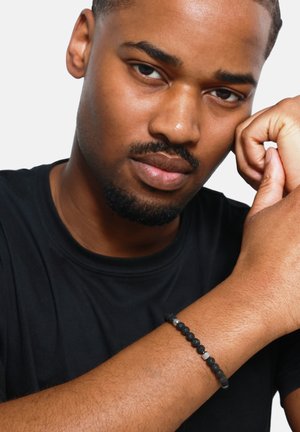 Black beaded bracelet featuring round matte black stones and silver accents, worn on the wrist of a person with dark skin.