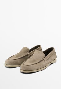 Mocassini in camoscio beige con dettagli cuciti e suola in gomma piatta. Presentano un design slip-on e una texture liscia.