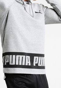 Grå hoodie av mjukt material. Har en svart logotyp på bröstet och ett djärvt svart band med "PUMA" i vitt vid fållen.