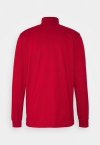 Červená polokošile s dlouhým rukávem, vysokým límcem, hladkou texturou a přiléhavými manžetami, s jednoduchým a čistým designem.