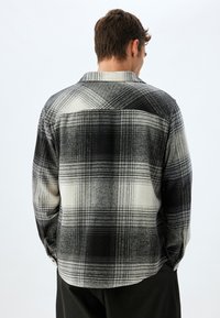 Camisa de franela a cuadros en blanco y negro con una textura suave, que presenta un collar tipo spread y puños con botones. La vista trasera muestra el detalle del patrón a cuadros.