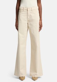 Pantalons larges beige en coton, dotés de poches avant, d'une taille haute et d'une texture lisse, assortis à des talons beige ornés.