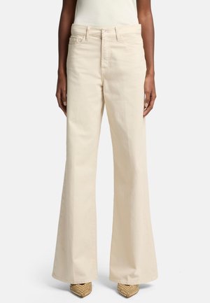 Pantaloni beige a gamba larga realizzati in cotone, dotati di tasche anteriori, vita alta e una texture liscia, abbinati a tacchi beige decorati.