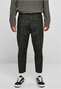 Pantalons en denim noir avec une coupe légèrement fuselée et une texture subtile. Portés avec des baskets noir et blanc et une chemise grise à manches longues.