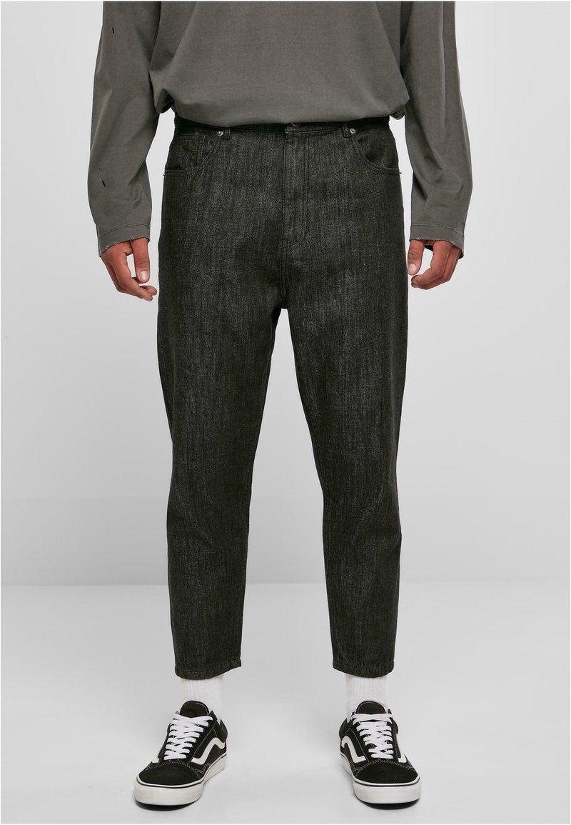 Pantalons en denim noir avec une coupe légèrement fuselée et une texture subtile. Portés avec des baskets noir et blanc et une chemise grise à manches longues.