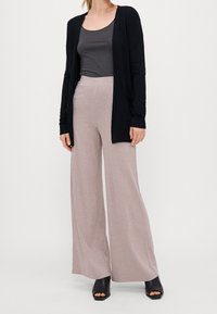 Cárdigan negro de manga larga, camiseta de tirantes gris y pantalones de pierna ancha de canalé en rosa claro; combinados con sandalias de tacón abierto negras.