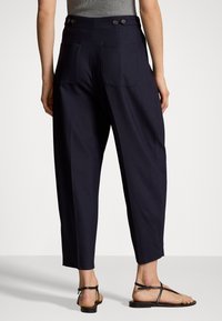 Marinblå vida byxor med två bakfickor, knappar i midjan och en slät yta. Kombineras med svarta platta sandaler.