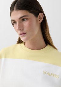Sweatshirt giallo e bianco con colletto a costine. Presenta ricami ondulati in giallo abbinato. Tessuto morbido e vestibilità casual.