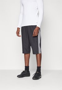 Graue Sportshorts mit weißen Seitenstreifen, kombiniert mit einem weißen Langarmoberteil und schwarzem Schuhwerk. Die Shorts haben eine lockere Passform.