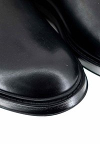 Scarpe in pelle nera con una superficie liscia, punta rotonda e un aspetto lucido. I bordi rinforzati e una lucentezza sottile esaltano la forma.