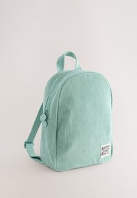 Sac à dos en velours côtelé vert menthe de forme arrondie, avec fermeture éclair, bretelles réglables et un écusson avant indiquant "PASSER UNE EXCELLENTE JOURNÉE."