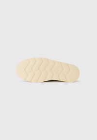 Sole of a light beige shoe with deep zigzag tread pattern, displayed against a plain white background.