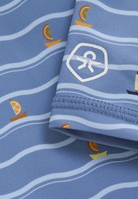 Blått tyg med vågiga linjer och små mönster av båtar och apelsinskivor. Inkluderar en vit logotyp på fållen. Slät och lätt textur.