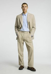 Bežna prilagojena obleka z svetlo modro črtasto srajco. Obleka ima strukturiran blazer in godrnjene hlače, v kombinaciji z rjavimi čevlji.