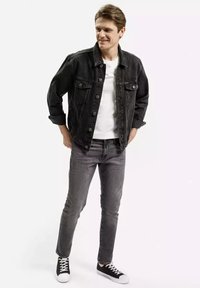 Czarna dżinsowa kurtka na białej koszulce, w zestawieniu z szarymi dopasowanymi dżinsami i czarnymi trampkami z białymi podeszwami. Prosty design i klasyczny krój.