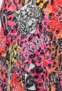 Haut à manches courtes coloré présentant un mélange d'imprimés animaliers en rose, orange, jaune et noir, avec une tête de tigre blanc et des accents en strass.