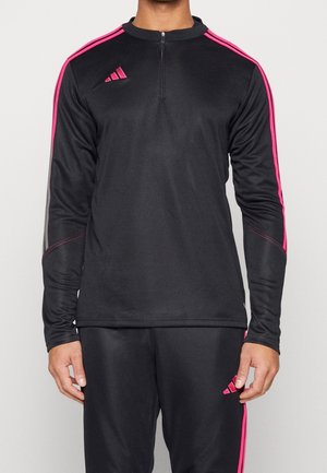 Schwarzer Sport-Trainingsanzug mit langen Ärmeln und Reißverschluss am Kragen, mit leuchtend pinken Streifen an Schultern und Beinen sowie pinkfarbenen Logos auf Brust und Oberschenkel.