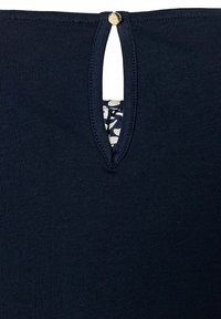 Marineblaues Oberteil mit einer Schlüsselloch-Öffnung auf der Rückseite, versehen mit einem goldenen Akzentknopf. Weicher, strukturierter Stoff mit einem gemusterten Innenfutter, das sichtbar ist.