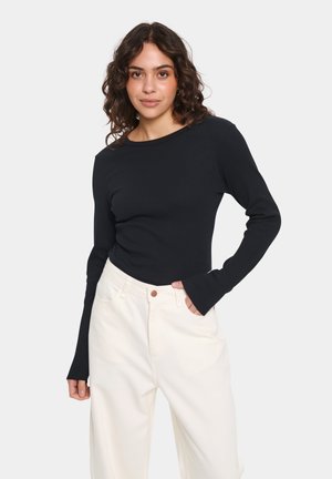 Zwart geribbeld top met lange mouwen, gemaakt van rekbare stof, met een ronde halslijn en een aansluitende pasvorm, gecombineerd met crème kleurige high-waisted broeken.