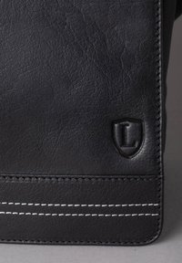 Black textured leather bag featuring white stitching and an embossed shield logo with "L" on the front. Smooth edges with structured design.