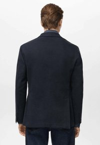 Sacou bleumarin cu croială ajustată, fente unică la spate și manșete cu trei nasturi; realizat din material texturat; asortat cu blugi albaștri.