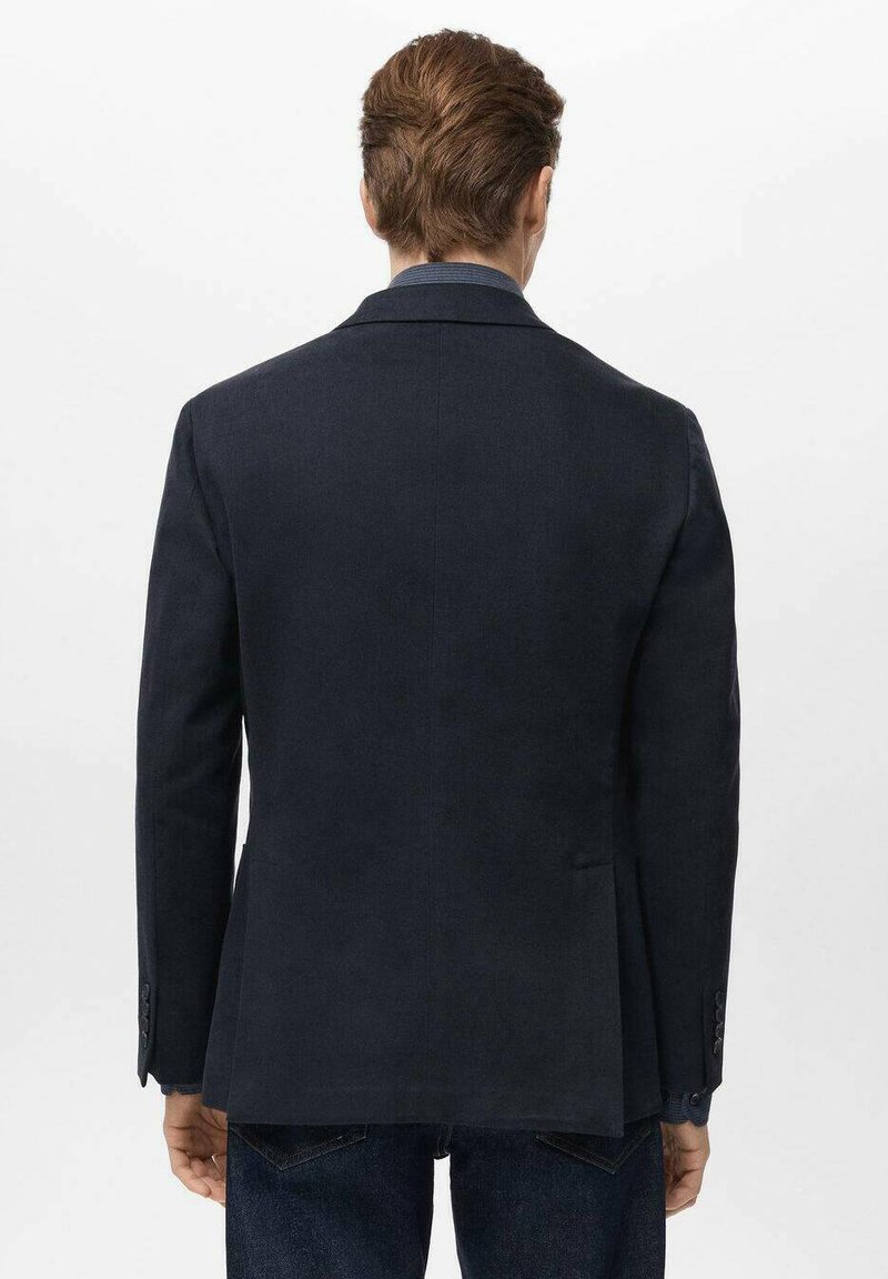 Marineblazer mit tailliertem Schnitt, kurzer Rückenschlitz und Dreiknopf-Manschetten; hergestellt aus strukturiertem Stoff; kombiniert mit blauem Denim.