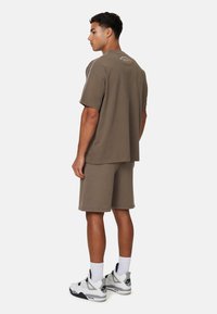 Olijfgroen katoenen T-shirt en shortset met een relaxte pasvorm. Witte stiksels en een logodetail op de achterkant. Draag het met witte sneakers.