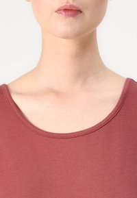 Top burdeos de escote redondo, hecho de una tela suave y ligera, con mangas cortas y una textura lisa, acabado limpio en el cuello.