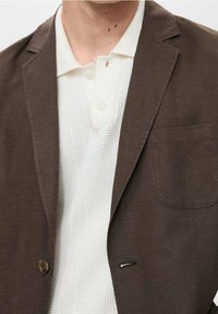 Brązowa marynarka z teksturowanym, kremowym swetrowym polo pod spodem. Marynarka ma kieszeń na piersi oraz ozdobne guziki.