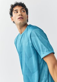 Kortärmad sport-t-shirt i ljusblått med ett strukturerat diamantmönster. Tillverkad av slätt tyg, med rund halsringning och avslappnad passform.