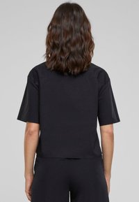 Czarny t-shirt z krótkim rękawem, wykonany z mieszanki bawełny, charakteryzujący się luźnym krojem i gładką teksturą. Segmentowany tył z zaokrąglonym dołem.