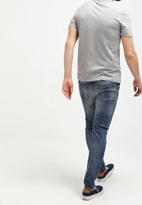 Camiseta gris de manga corta, vaqueros azul denim y zapatillas náuticas azul marino con detalles naranjas, vistas desde atrás, mostrando un conjunto casual.
