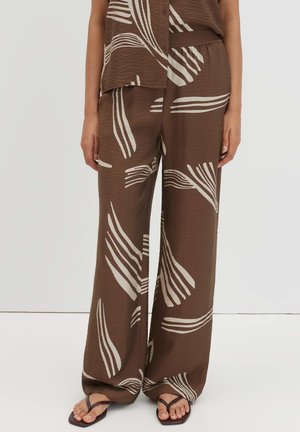 Braune weit geschnittene Hose mit weißen abstrakten Blattmustern, kombiniert mit passendem Oberteil und dunkelbraunen Sandalen.