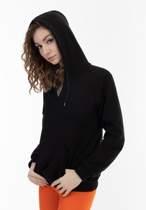 Felpa nera con scollo a V, maniche lunghe, tasca frontale e cordoncino regolabile. Tessuto leggermente testurizzato. Il modello indossa leggings arancioni.