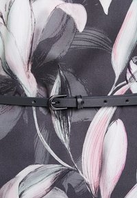 Tissu à motif floral avec des nuances de gris, rose et noir, doté d'une fine ceinture en cuir noir avec une boucle métallique à la taille.